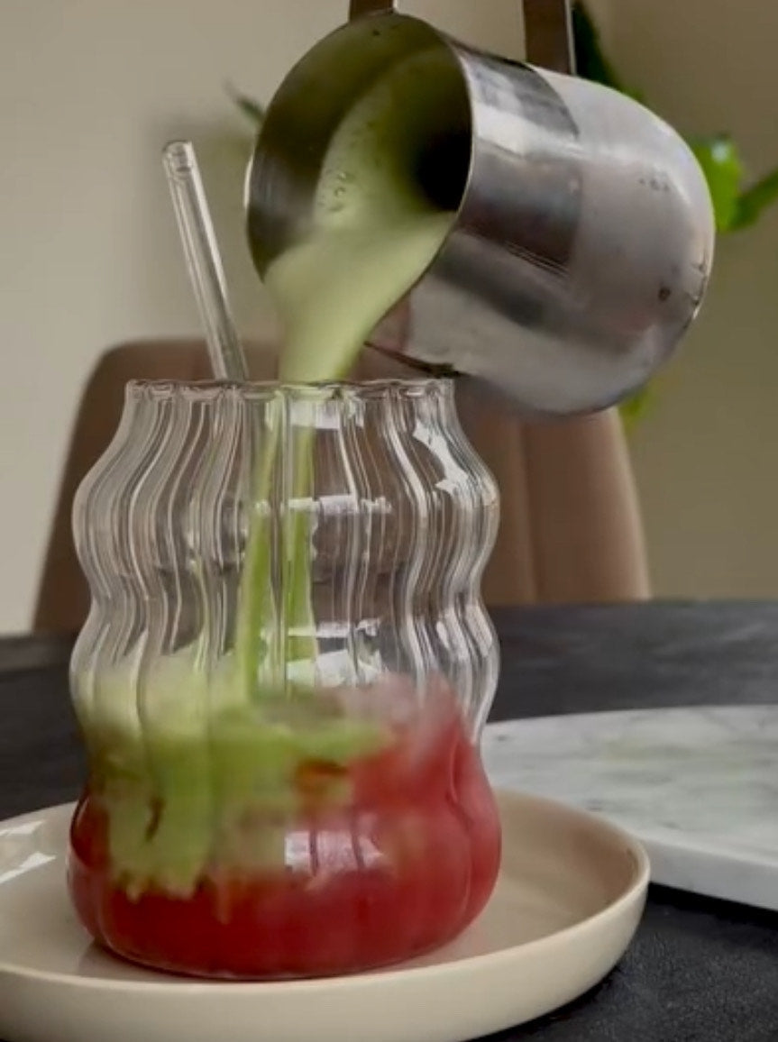 Iced strawberry matcha latte in een glas met ijs, met een roze aardbeienlaag onderaan en groene matcha bovenaan